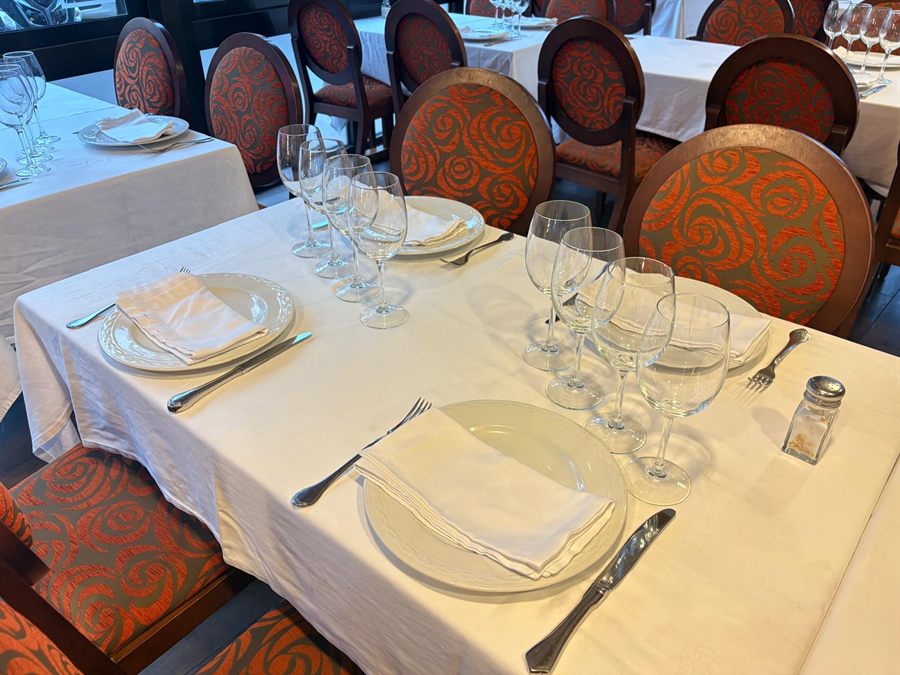 Mesa vestida con mantel de lino blanco, vajilla y copas en la sala de Bell Port